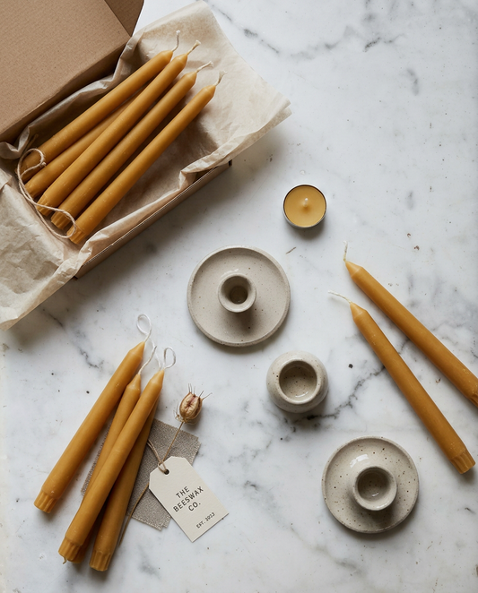 Beeswax candles and ceramic holders on a marble surface with a visible brand tag.